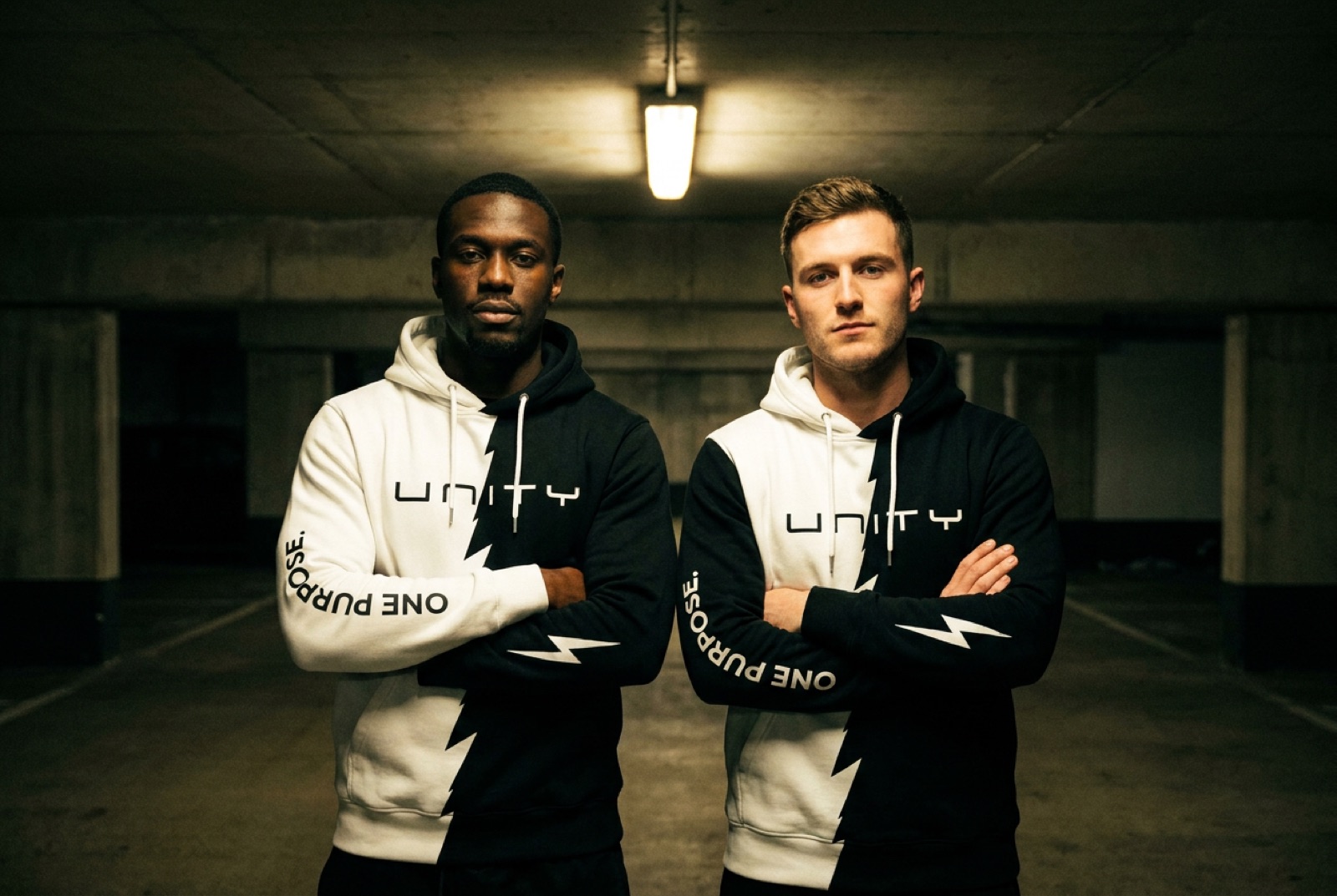 Two models, one Black and one white, shoulder to shoulder in mirrored UNITY split hoodies
